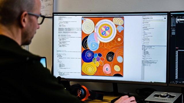 En person sitter vid en dator med en tavla av Hilma af Klint.