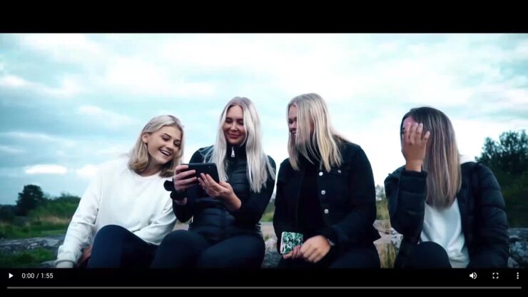 En grupp unga kvinnor tittar skrattande på en mobiltelefon utomhus