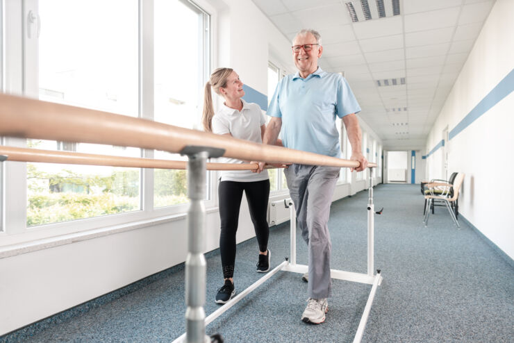 En fysioterapeut gångtränar med en äldre man i en korridor